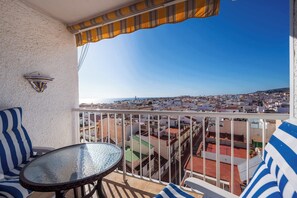 Ein Balkon mit Tisch und Stühlen, Blick auf eine Stadtlandschaft und ein gestreiftes Markisen