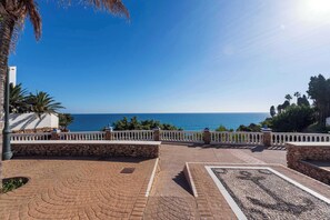 Eine gepflasterte Terrasse mit einer Steinmauer, einer Palme und Blick auf das Meer.