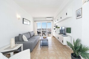 Una sala de estar moderna con un sofá gris, una mesita, un televisor y un balcón con vistas.