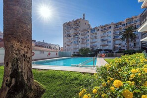 Una piscina rodeada de vegetación y un edificio de varios pisos con balcones.