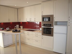 A modern kitchen with white cabinets, a stainless steel oven, a microwave, and a white refrigerator. - Hernan Cortes (Nerja)