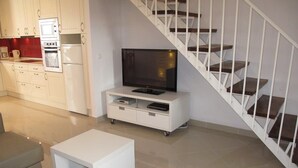 A modern living room with a flat-screen TV, a white entertainment unit, a sofa, and a staircase. - Hernan Cortes (Nerja)