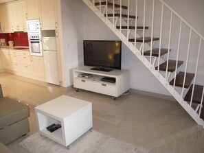 A modern living room with a flat-screen TV, a white entertainment unit, a sofa, and a staircase.