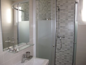Un baño moderno con cabina de ducha de vidrio, un lavabo blanco y un espejo sobre él.