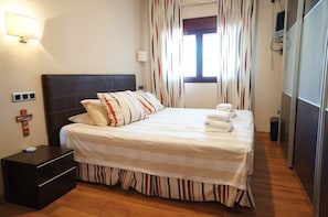 A hotel room with a bed, bedside table, curtains, and a window.