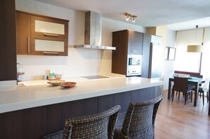 A modern kitchen with a central island, dark cabinetry, and a dining area with chairs. - Carabeo 1-30 (Nerja)