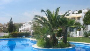 A swimming pool with a circular island, palm trees, and a white building in the background. - Paraiso Blanco (Nerja)