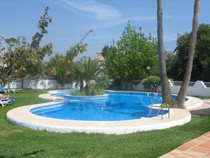 A swimming pool with a circular design, surrounded by grass and palm trees. - Paraiso Blanco (Nerja)