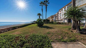 A beachfront hotel with palm trees, a clear sky, and a view of the ocean.