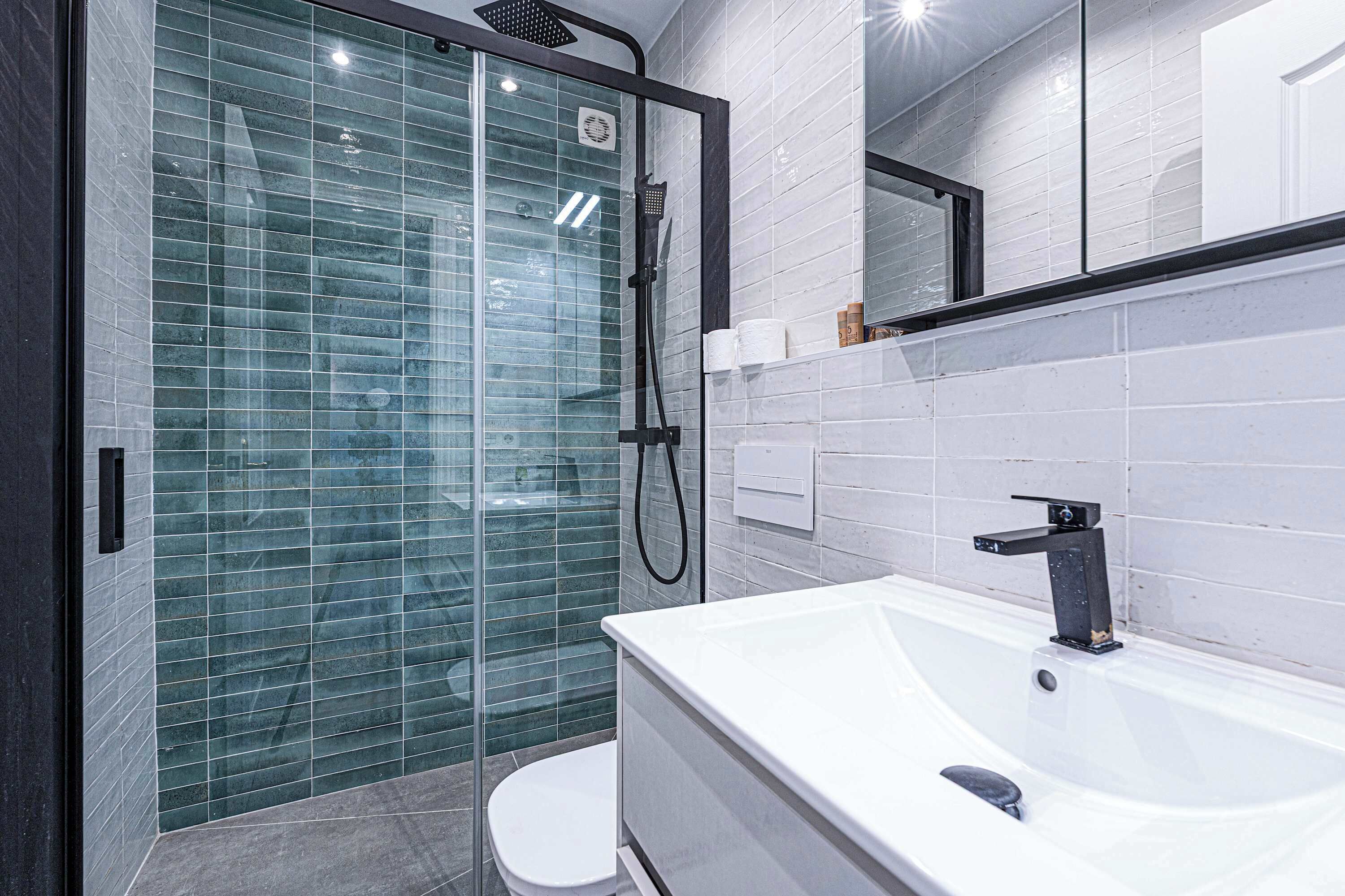 A modern bathroom with a glass shower enclosure, a white bathtub, and a large mirror above the sink.