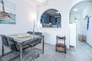 A modern kitchen with blue cabinets, a dining area with a glass table, and a view of the sea through a painting. - Jardines del Mar (Torrox)