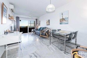Ein modernes Wohnzimmer mit einer Couch, einem Esstisch und Stühlen, einem Balkon mit Blick und Kunstwerken an den Wänden.