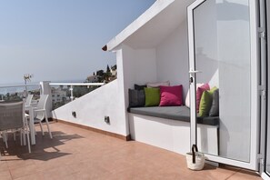 A balcony with a seating area, a table with chairs, and a view of the city.
