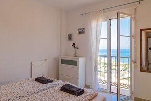 A bedroom with a bed, a dresser, a window with a view, and a door leading to an outdoor balcony.