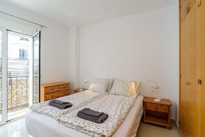 Un dormitorio con una cama, mesitas de noche, un armario de madera y un ventanal corredero que da a un área exterior.