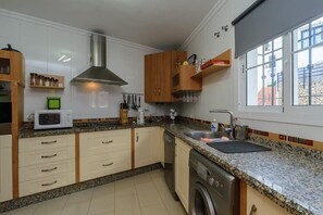 A kitchen with granite countertops, a stainless steel range hood, wooden cabinets, a dishwasher, and a window with a view of the outside.