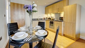 Una cucina moderna con mobili in legno, un tavolo da pranzo per quattro con piatti bianchi e posate, e un vaso con fiori viola.