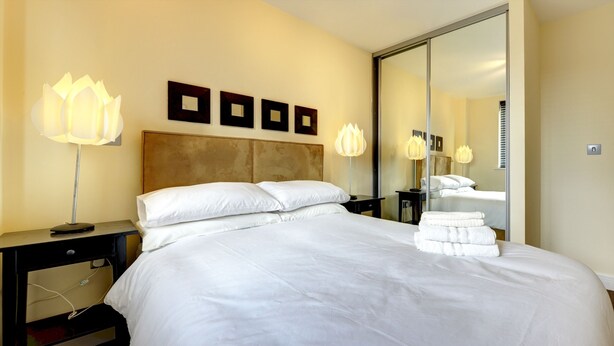 Camera d'albergo con un letto grande, un comodino con una lampada, uno specchio e una parete con quadri.