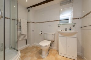 A bathroom with a glass shower enclosure, a toilet, a sink with a mirror above it, and a towel rack. - Self-Catering Farmhouse Cottage set in the Dorset Countryside (Pet Friendly) (West Milton)