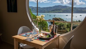 Een tafel met een bord eten, een vaas bloemen en een metalen bak, met uitzicht op een meer en boten door een groot raam.