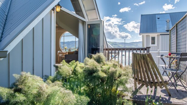 Een modern huis met een terras met uitzicht op een wateroppervlak, een houten stoel en een tafel met een lamp.