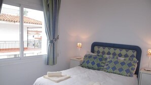 A neatly made bed with folded towels, a patterned headboard, and bedside lamps. - Edf Malaga (Nerja)