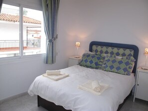 A neatly made bed with folded towels, a patterned headboard, and bedside lamps. - Edf Malaga (Nerja)