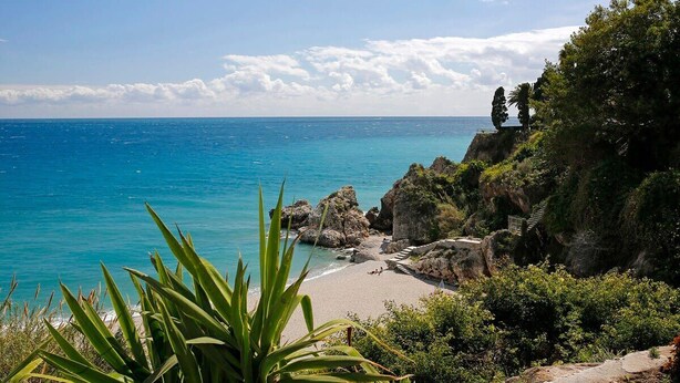 A coastal landscape with a beach, rocky terrain, and vegetation. - Edf Malaga (Nerja)