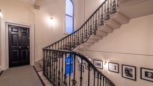 Un'imponente scalinata con ringhiere in ferro nero decorate, una porta nera con un mazzo di ottone e quadri appesi alle pareti.