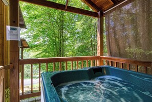 Een houten terras met een jacuzzi en uitzicht op een bos.