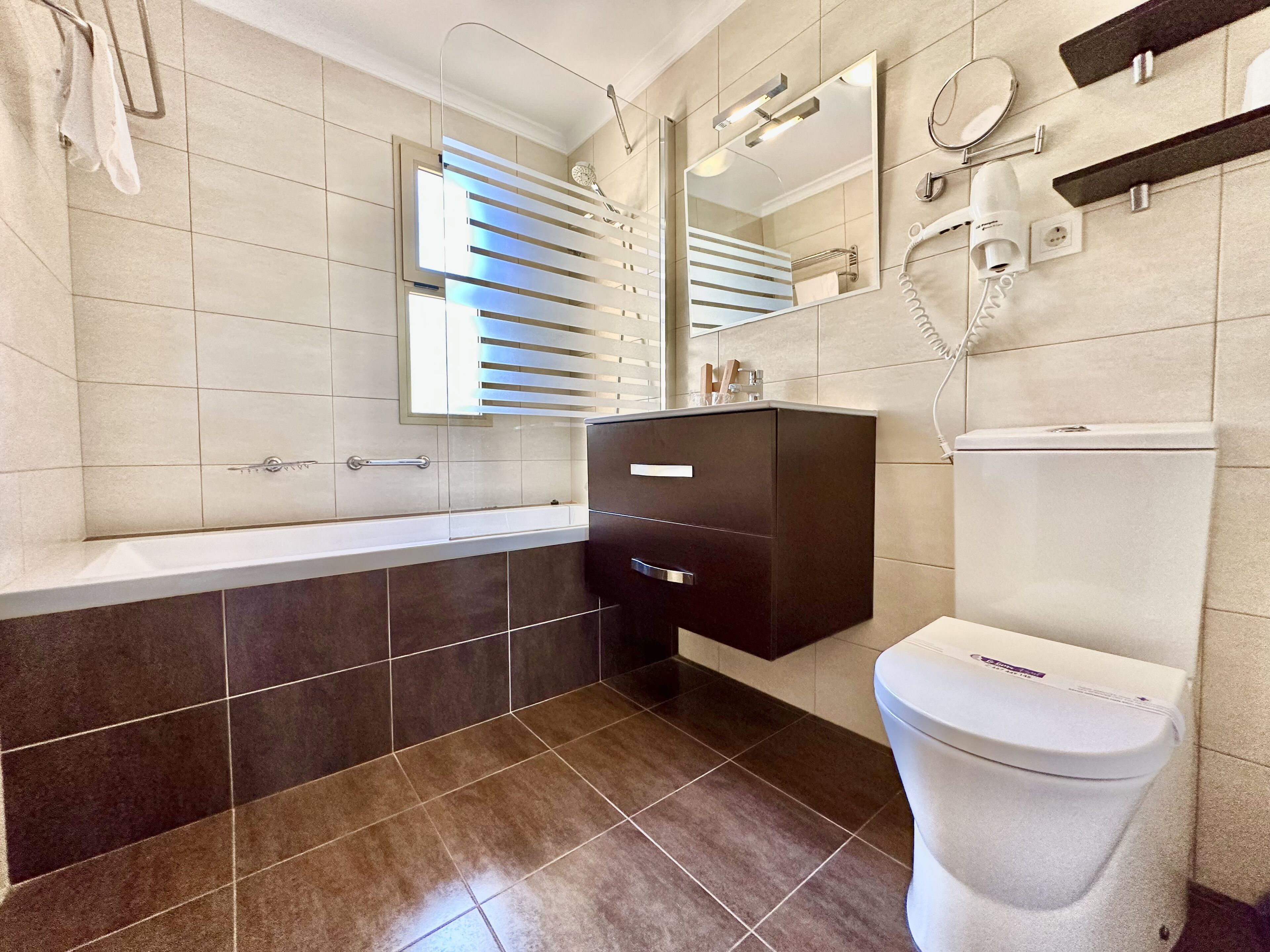 A modern bathroom with a bathtub, a toilet, a vanity with a mirror, and a hairdryer on the wall.