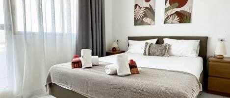 A hotel room with a large bed, a bedside table, a lamp, and a window with curtains.