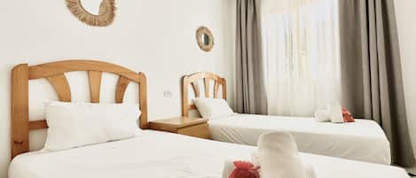 A hotel room with two beds, a wooden headboard, a small bedside table, a mirror, and a window with curtains.