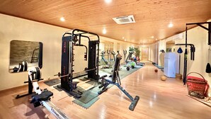 Et rummeligt fitnesscenter med forskellig træningsudstyr, herunder en squat-stander, løbebånd og vægte.