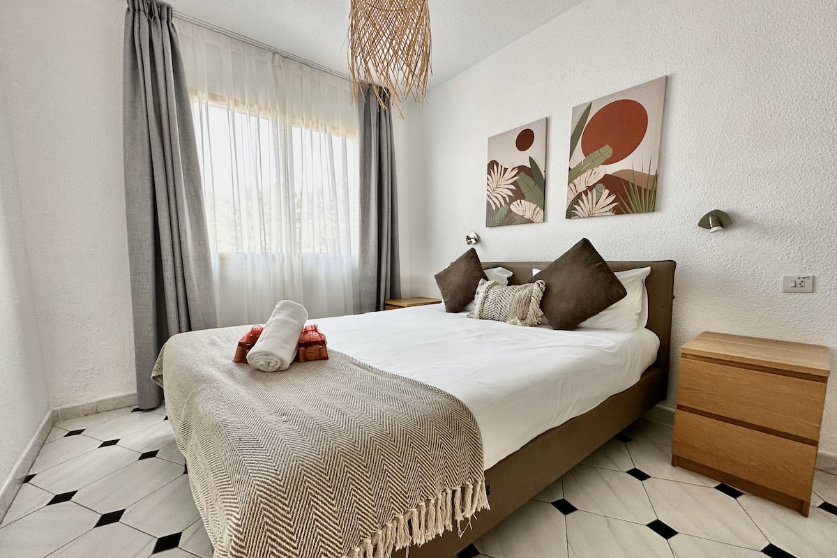 Une chambre à coucher moderne avec un grand lit, une table de chevet en bois et une décoration murale.