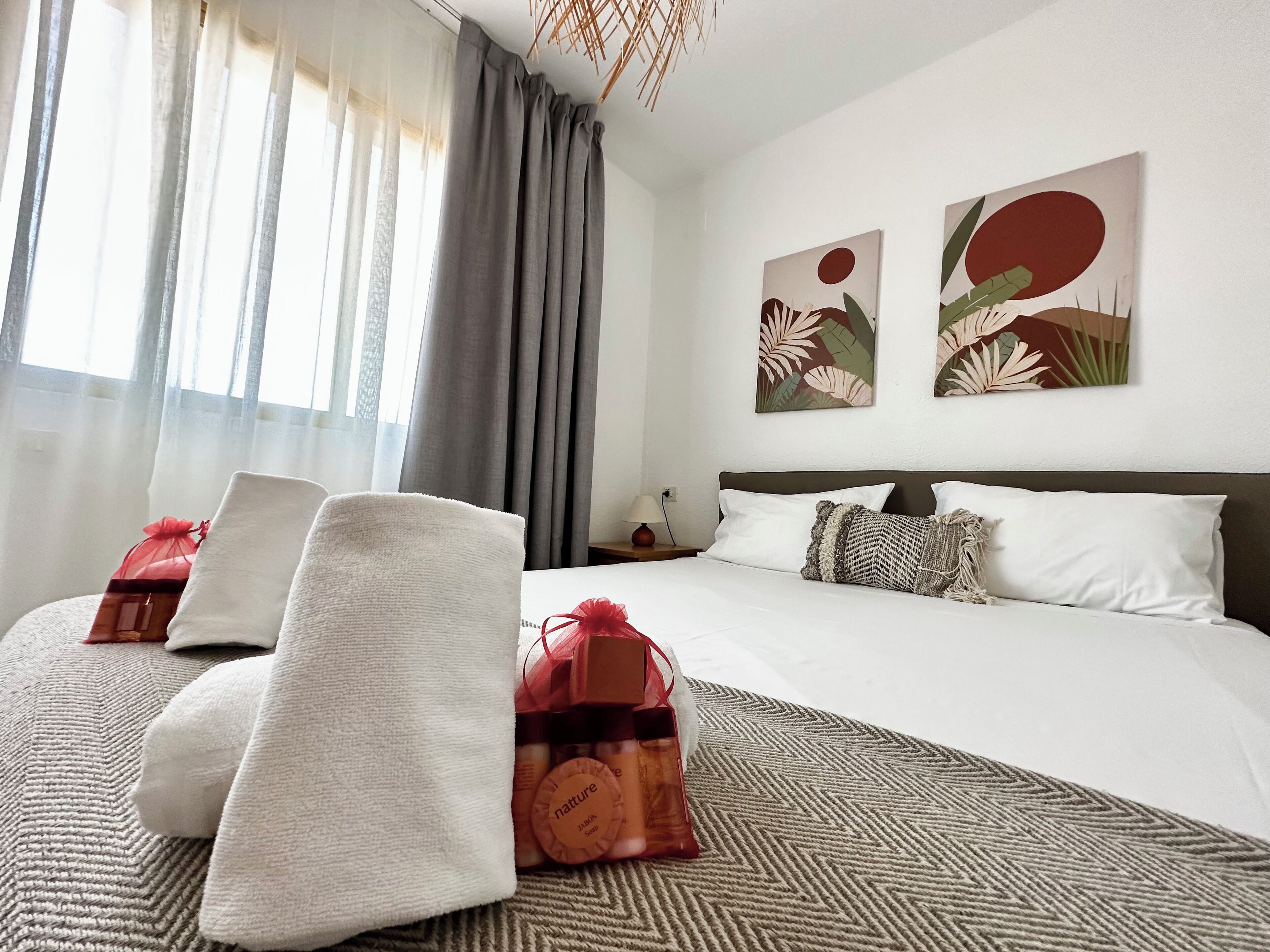 A hotel room with a neatly made bed, a large window with curtains, and two wall art pieces.