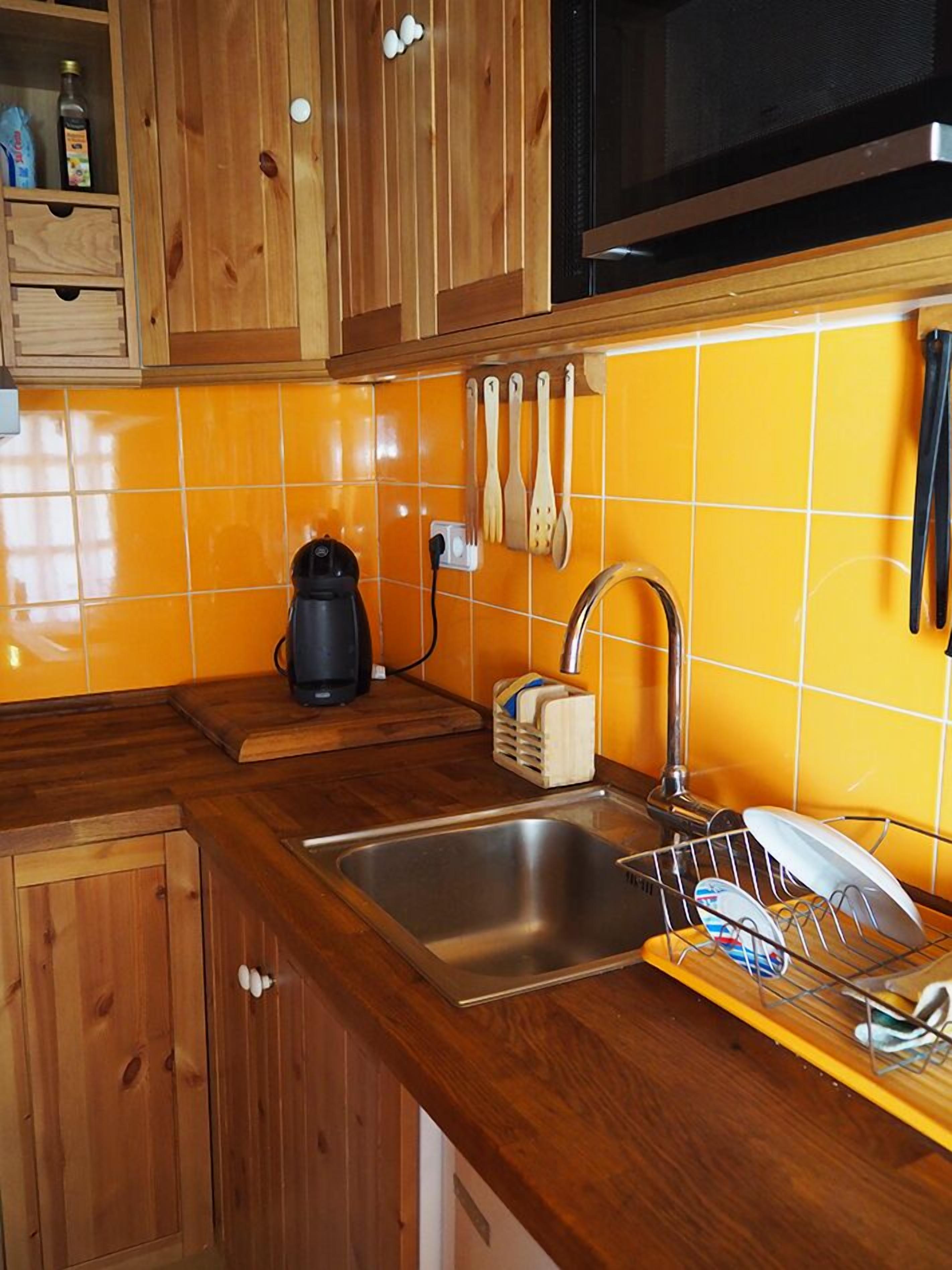 Een keuken met houten kastjes, een roestvrijstalen spoelbak, een koffiezetapparaat en een afwasschuurrek.