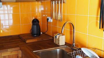 Una cocina con armarios de madera, un lavamanos de acero inoxidable, una cafetera y un escurreplatos.