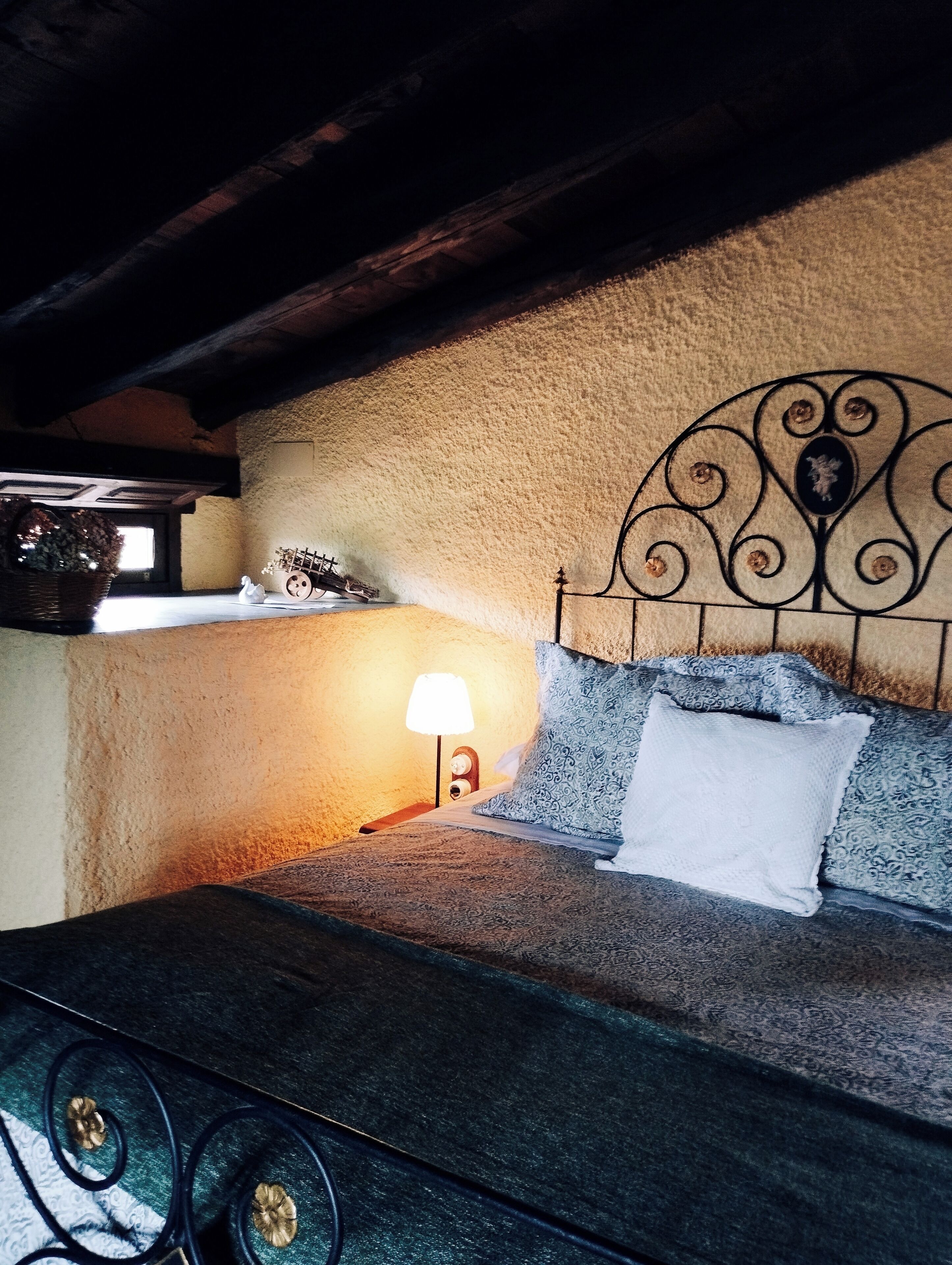 Un dormitorio acogedor con pared de piedra rústica, cabecero de metal y ropa de cama estampada.