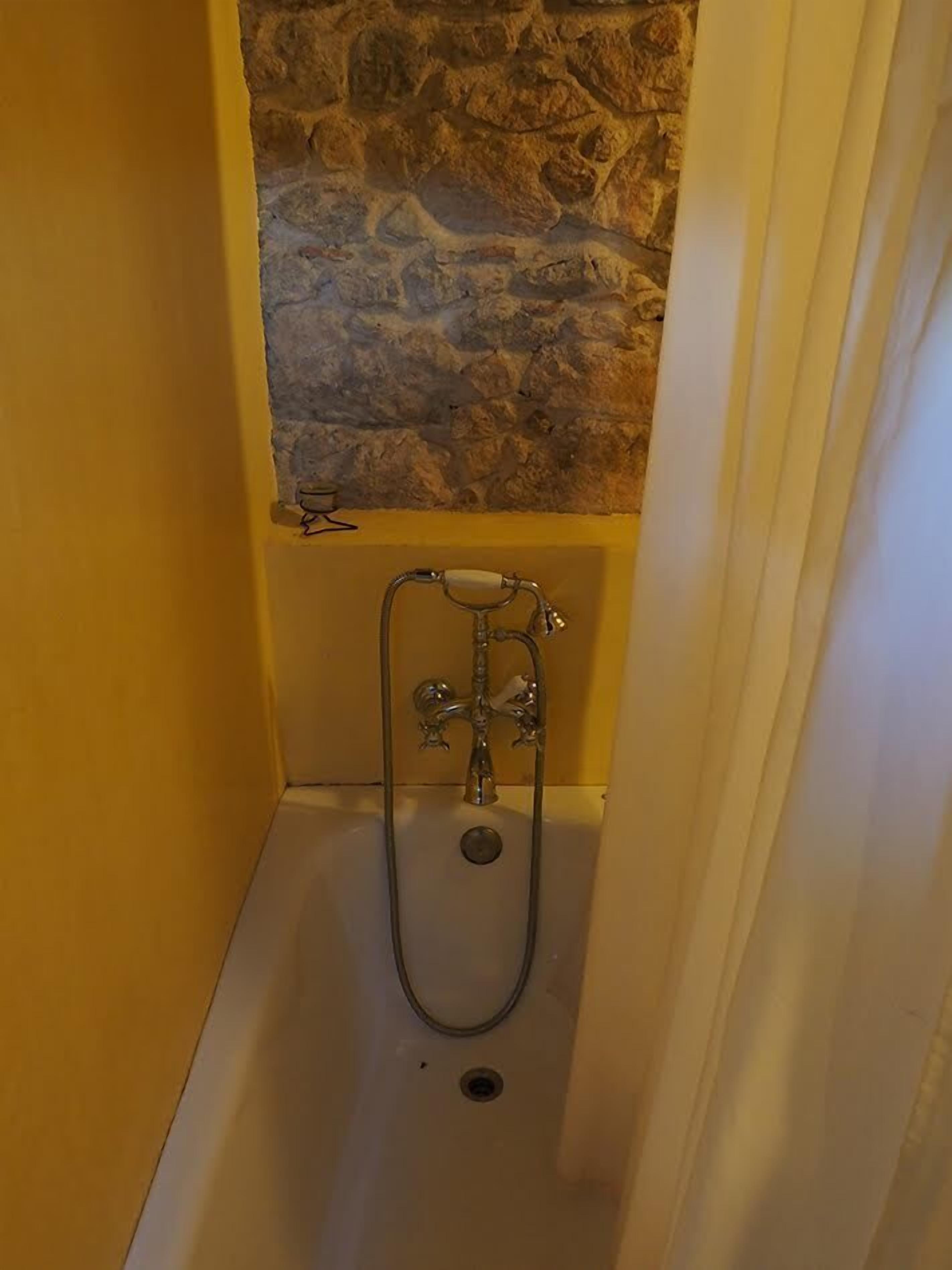 Un baño pequeño y cerrado con pared de piedra, una bañera y un cabezal de ducha.