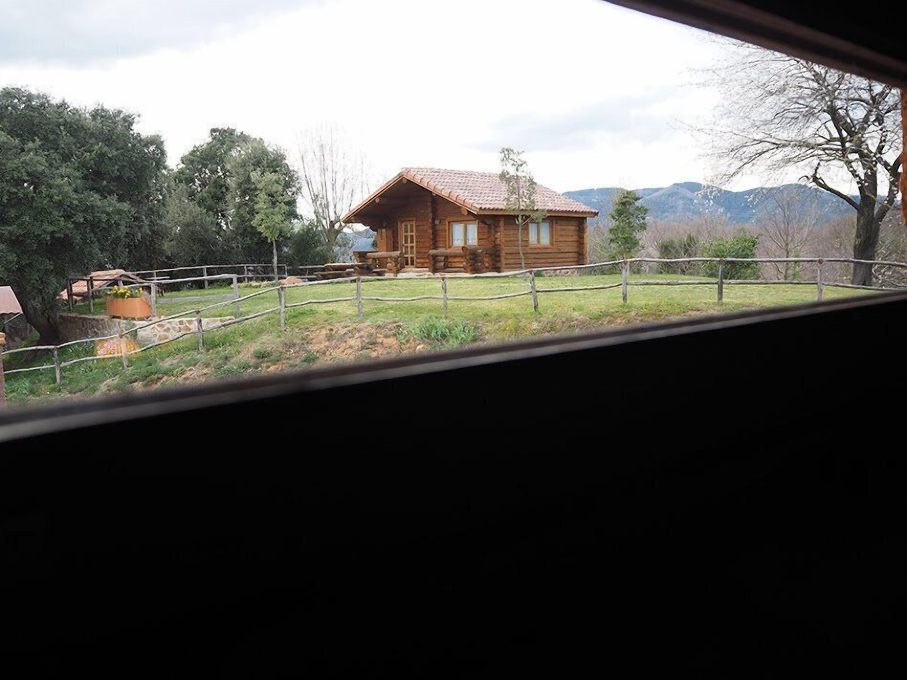 Een rustieke houten chalet met pannendak, omgeven door een omheinde tuin en bomen.