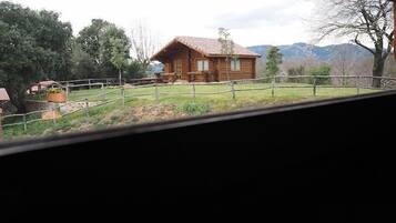 Een rustieke houten chalet met pannendak, omgeven door een omheinde tuin en bomen.