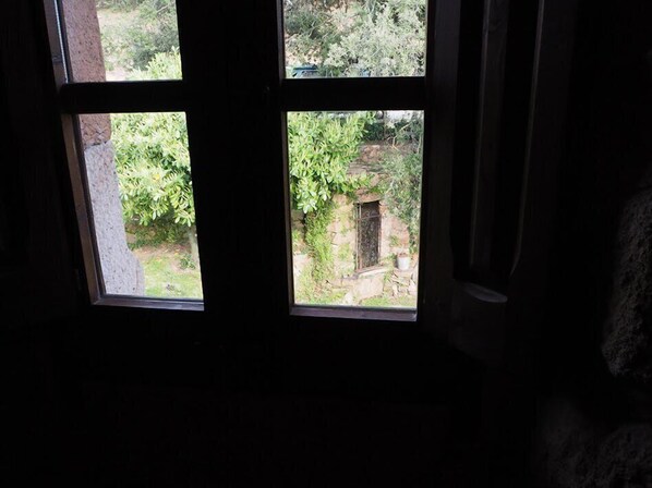 A window with a view of a garden and a stone structure. - Mas Cal Sastre (Sant Hilari Sacalm)