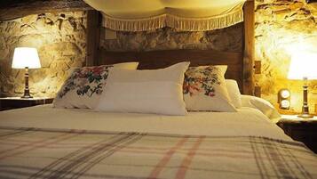 A bed with floral pillows, a plaid blanket, and a stone wall backdrop.