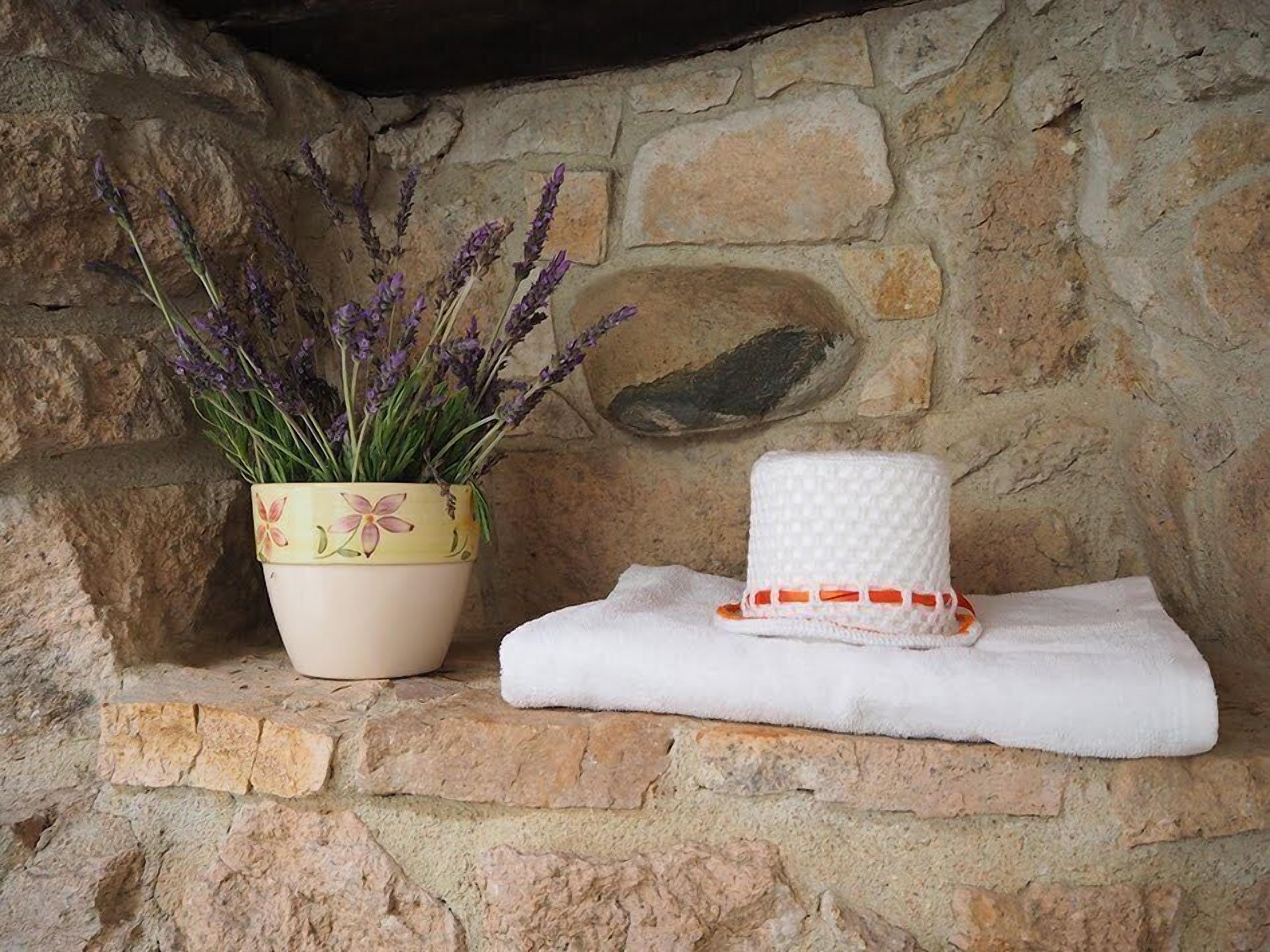A stone wall with a potted lavender plant and a white towel with orange trim.