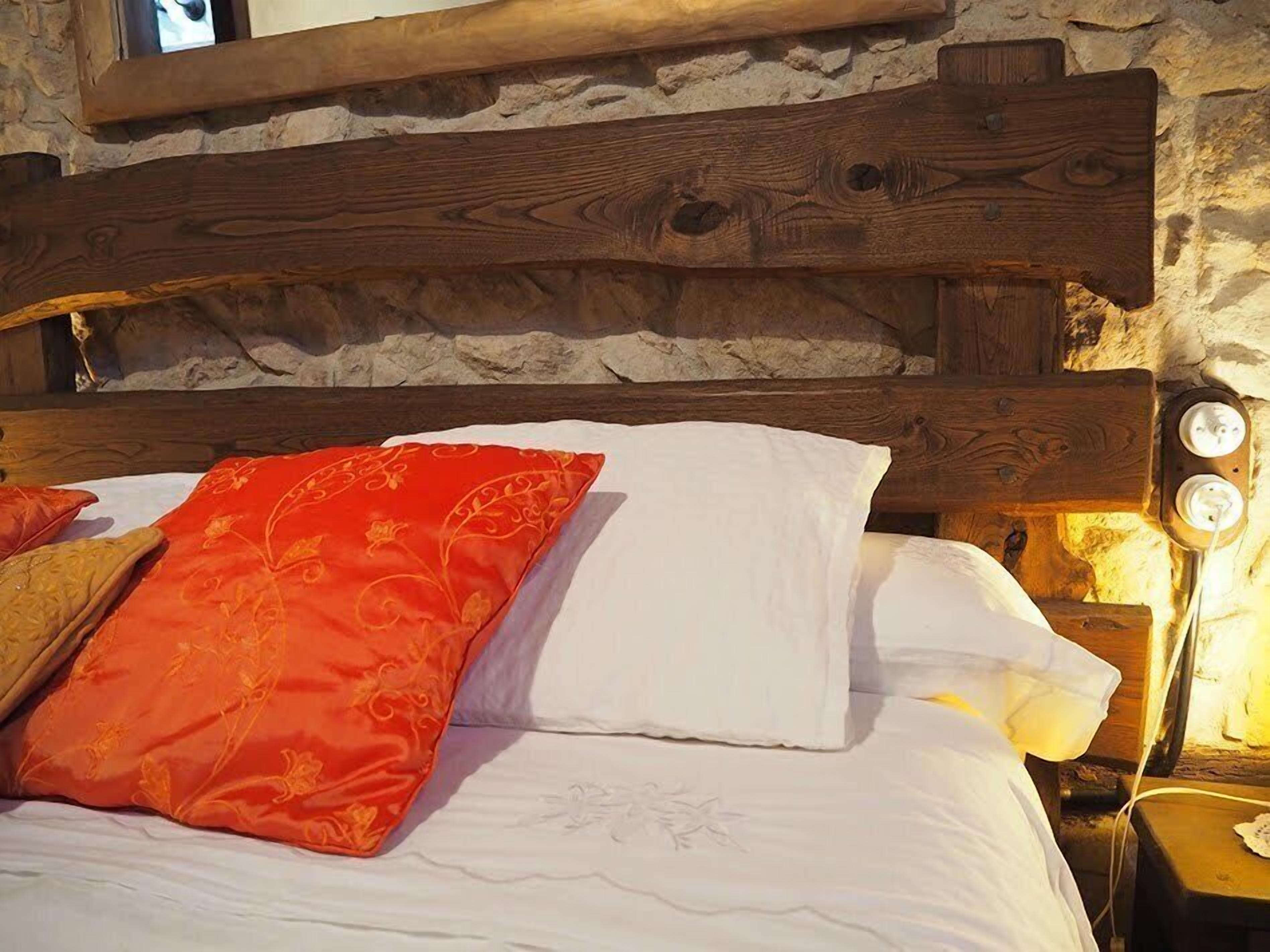 A bed with a wooden headboard, white and red pillows, and a nightstand with a lamp.