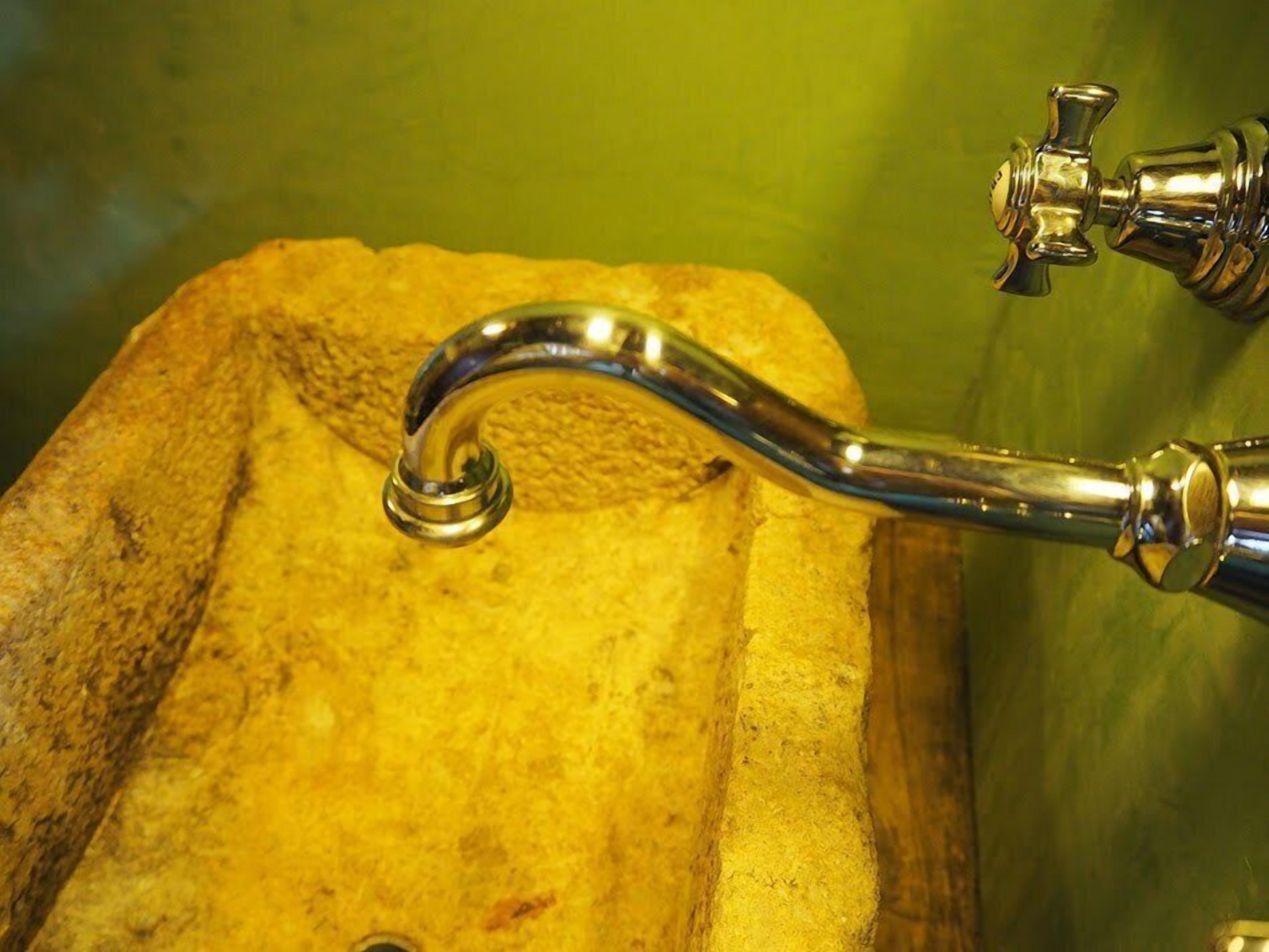A metal faucet with a curved spout attached to a stone sink.