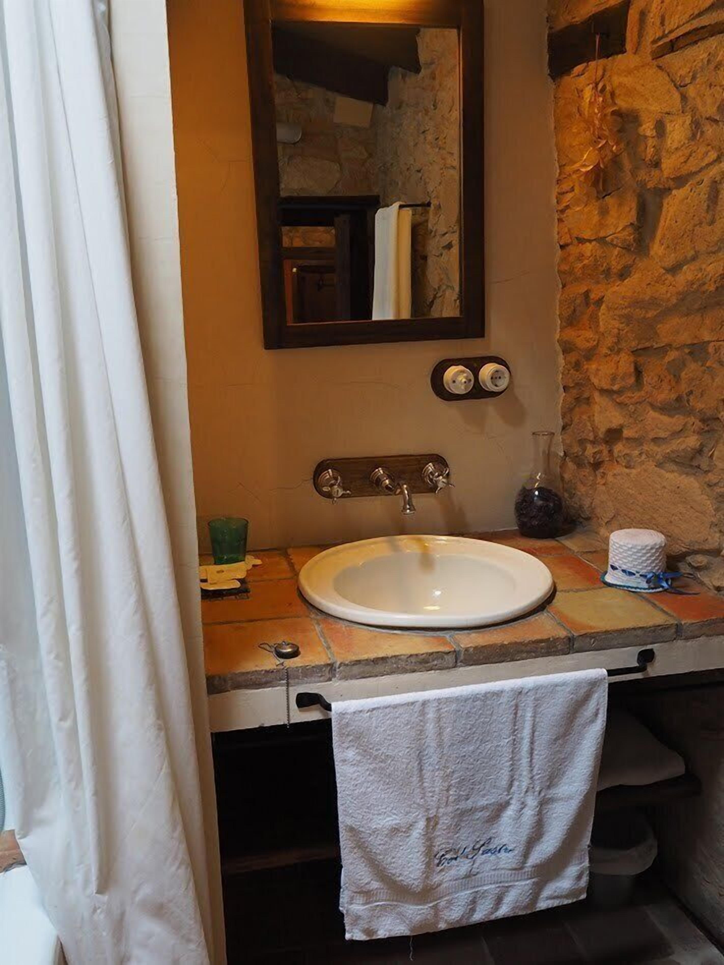 A bathroom with a stone wall, a white sink, a mirror, and a towel hanging on the wall.