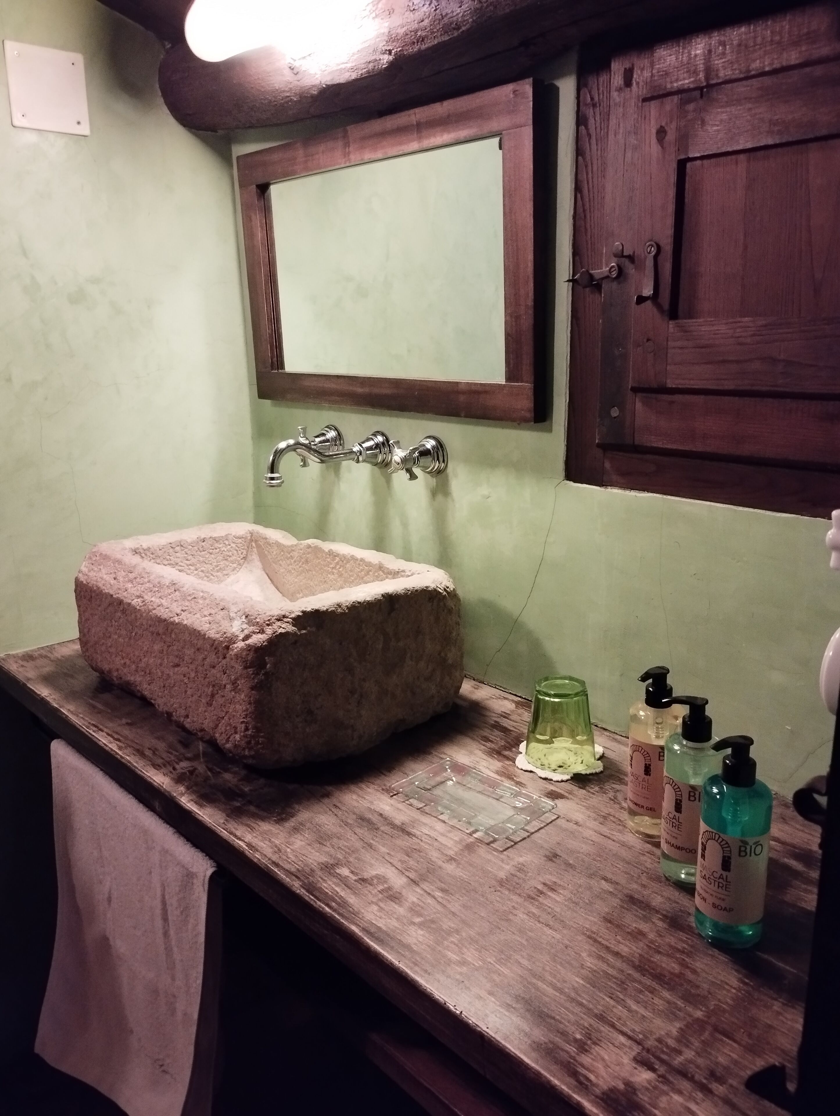 Un baño con un lavabo de piedra, encimera de madera y un espejo encima. Hay artículos de aseo en la encimera.