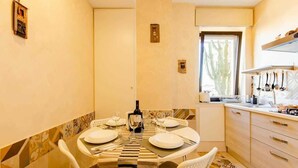 A dining area with a round table set for four, a window with a view, and a kitchen area with utensils hanging above the counter. - The House of the Pine Nativity (Napoli)